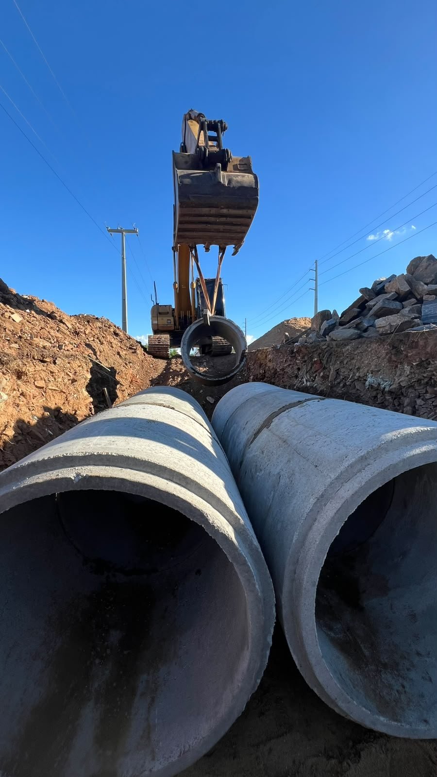 Escavadeira içando tubo de concreto para a rede de drenagem